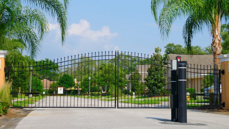 Entrance gate to a beautiful gated private community with lush green trees and grass.
