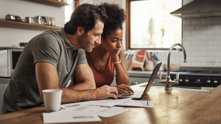 Laptop, couple and financial planning in a kitchen with mortgage documents learning about qualified versus nonqualified mortgages.