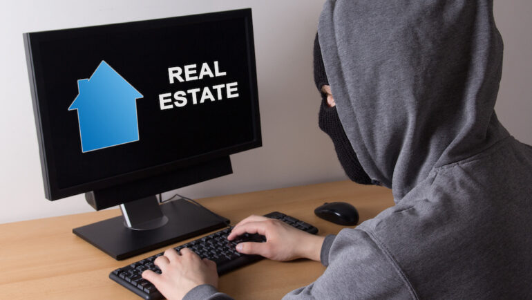 Cybercriminal committing home title theft. Photo of a thief in a mask searching for information about real estate online.